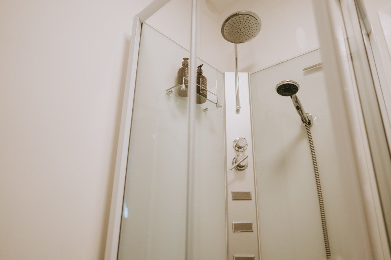 Une douche équipée d’un pommeau de douche à main, d’un robinet mural et d’un panneau de commande avec des boutons et un cadran de réglage de la température.