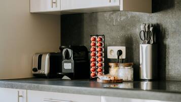 Un piano di lavoro in cucina con un tostapane, una macchina per il caffè, un vasetto di marmellata, un contenitore di posate e una presa elettrica.