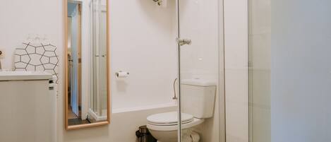 A modern bathroom with a toilet, a shower enclosure, and a mirror.