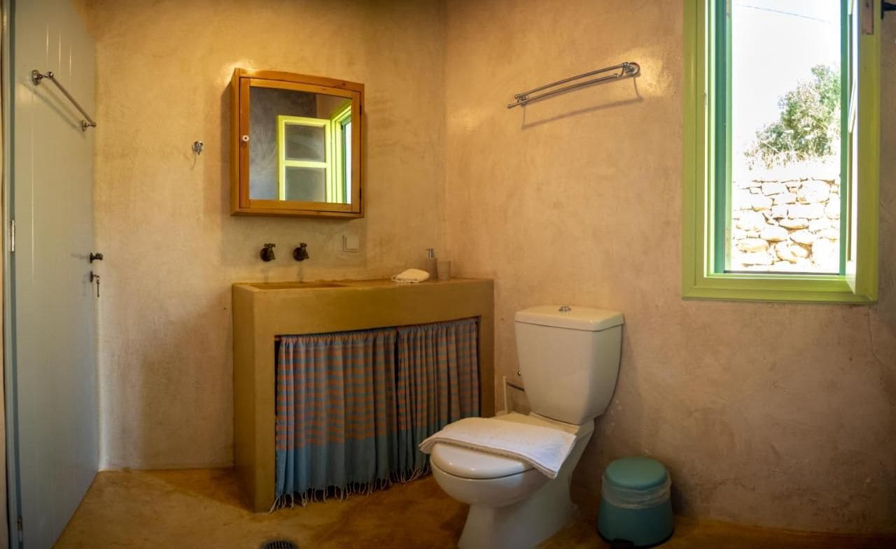 Et badeværelse med toilet, håndvask, spejl og et vindue.