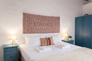 Een net opgemaakt bed met witte lakens, een patroonrijk wandtapijt erboven en twee nachtkastjes met lampen.