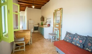 A compact kitchen with a dining area, a wooden bench, and a sofa with patterned cushions.