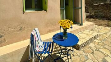 En bygning med en stenbelagt terrasse, et blåt bord med en vase med gule blomster, og et stribet håndklæde på en stol.