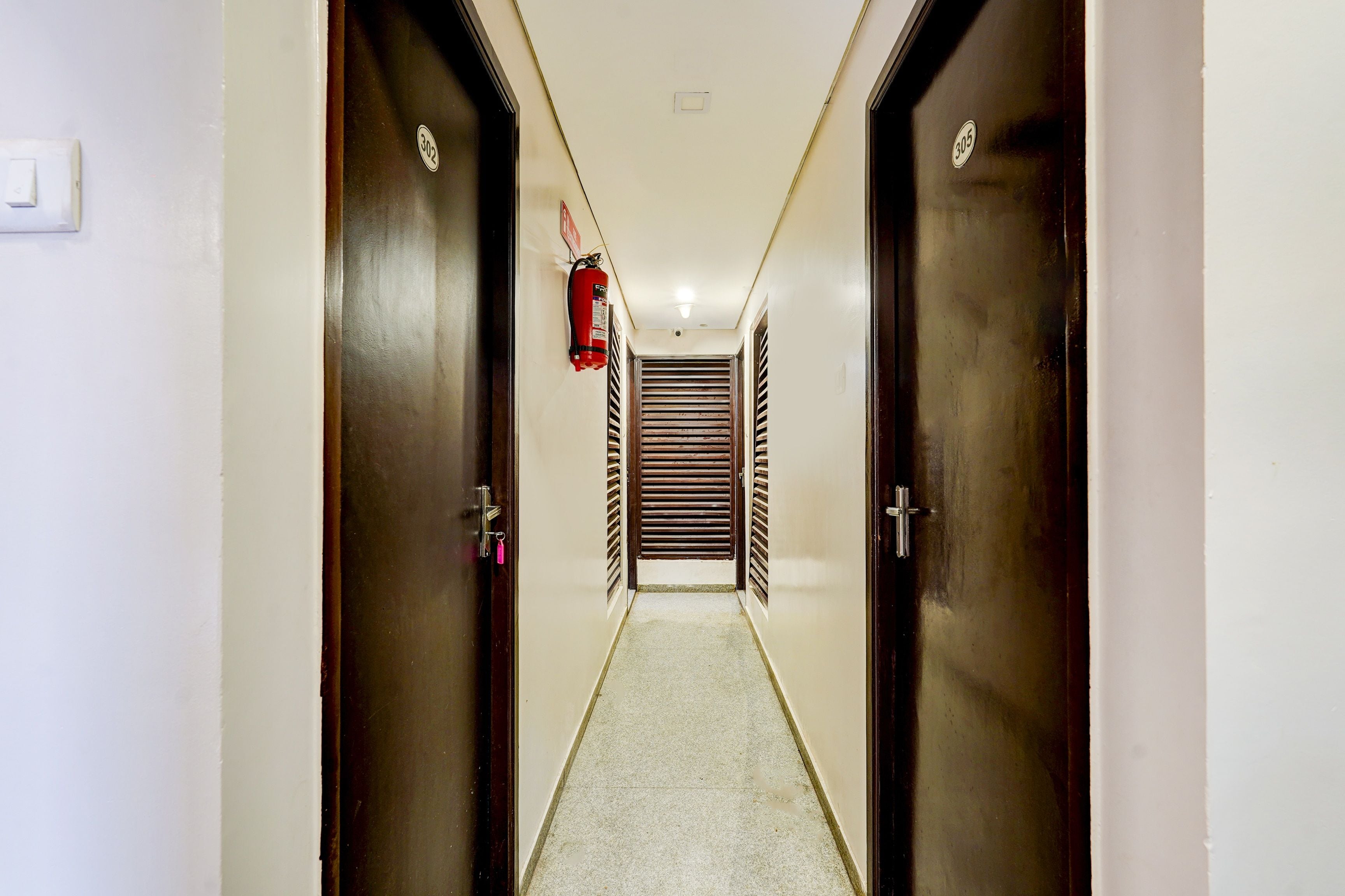 A hallway with two doors, a fire extinguisher, and a vented wall.