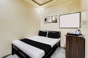 A hotel room with a bed, a bedside table with a kettle, and three framed pictures on the wall.
