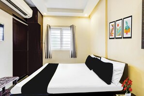Habitación de hotel con una cama, ventana con cortinas, aire acondicionado montado en la pared y cuadros enmarcados.