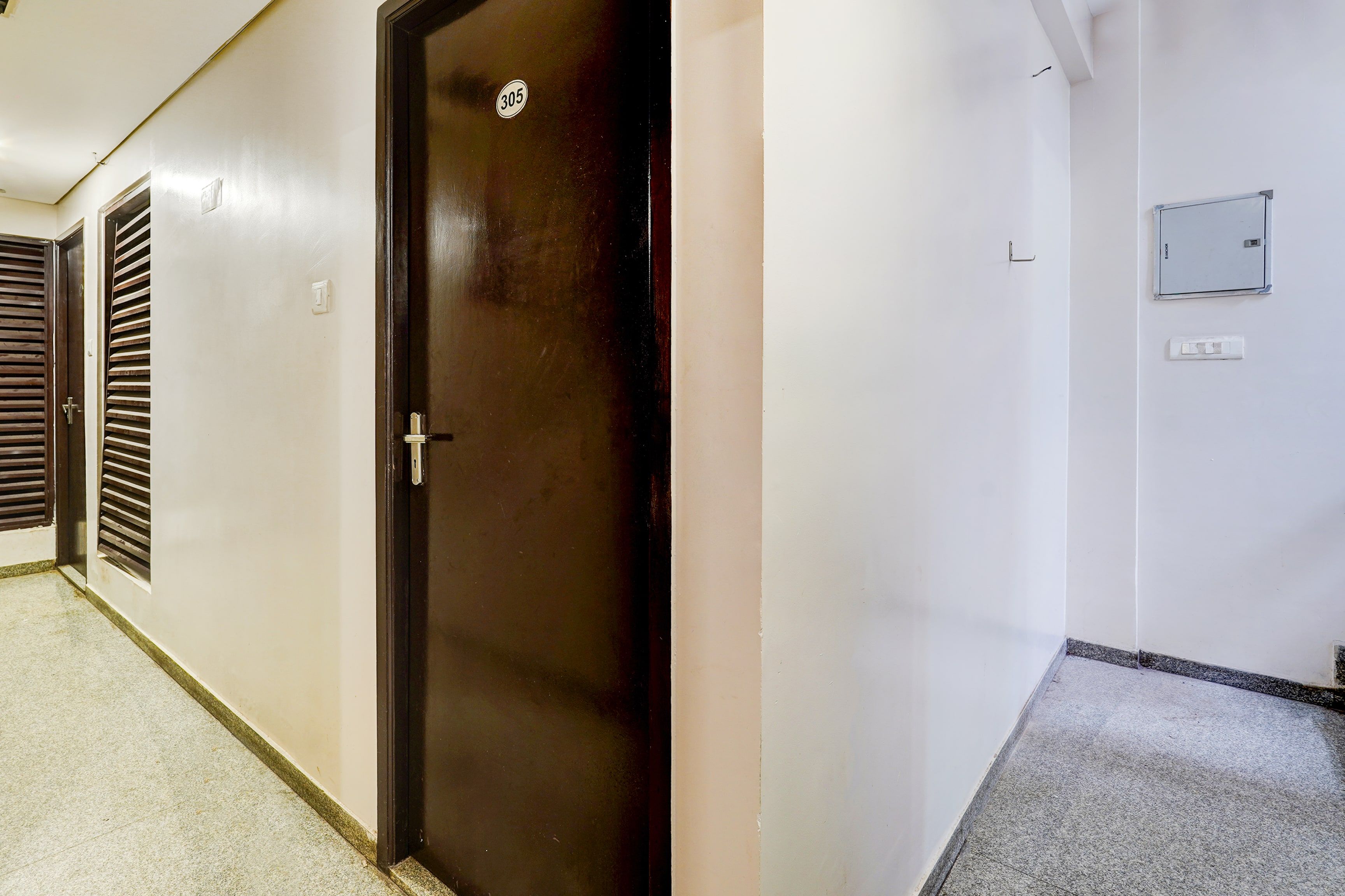 Un pasillo con una puerta cerrada marcada con el número 305, un interruptor de luz y un cuadro eléctrico de pared.
