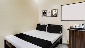 Una habitación de hotel con cama, una mesita de noche de madera y televisor montado en la pared.
