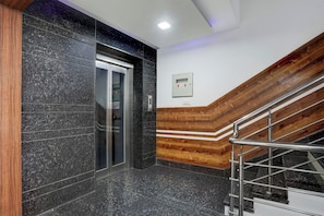 Un ascensor moderno con detalles metálicos, paneles de madera en la pared y una escalera de metal con barandilla.