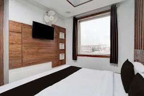 Habitació d'hotel amb un llit, una televisió penjada, un ventilador de sostre i una finestra amb cortines.