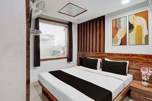 A hotel room with a bed, a window, a fan, a wooden headboard, and a wall with artwork. - Hotel O KSR Bengaluru City Junction (Bengaluru)