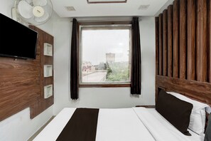 Habitació d'hotel amb llit, televisió, finestra amb cortines i vista sobre el paisatge urbà.