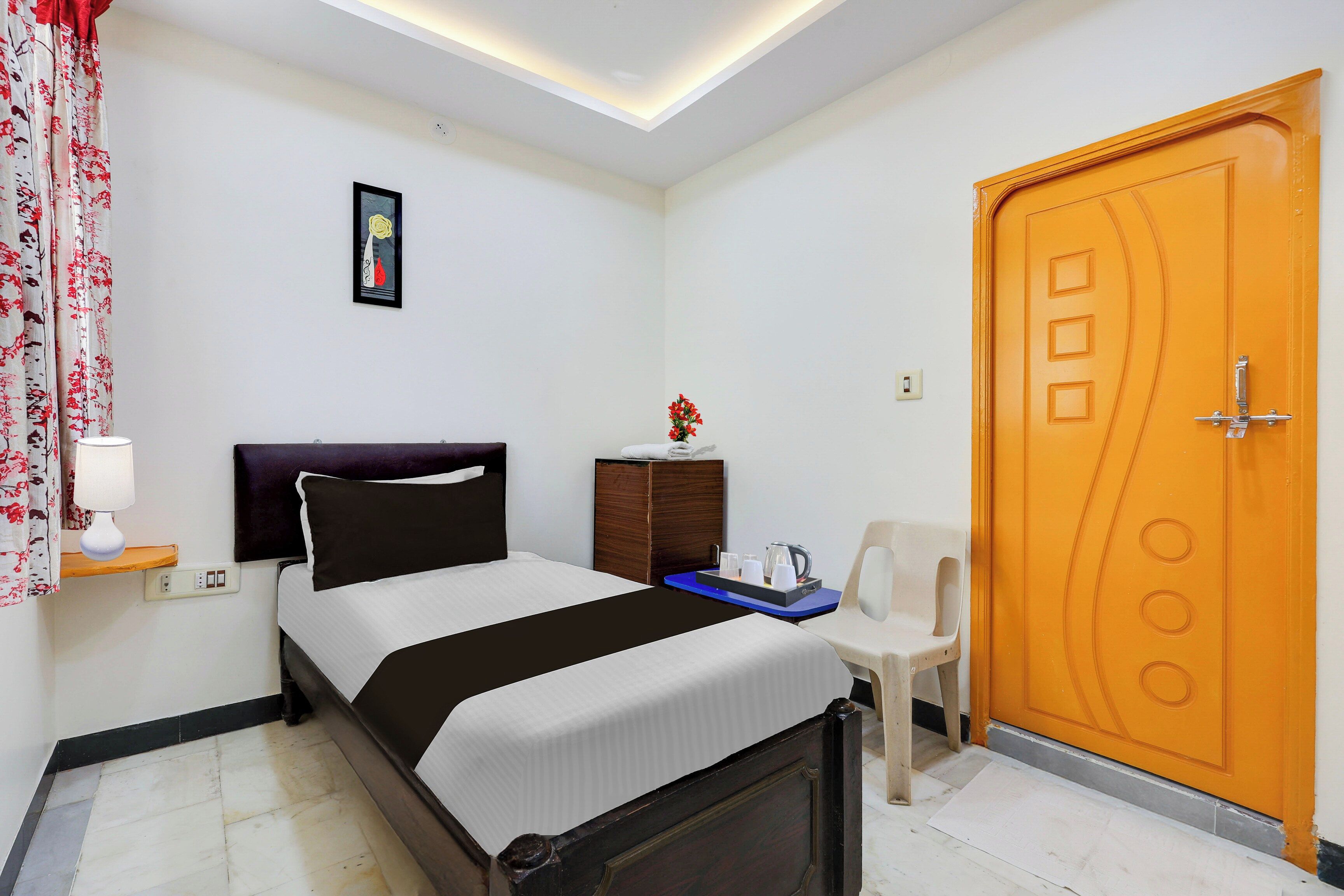 Una habitación de hotel con cama, escritorio con tetera, silla, puerta y un cuadro colgado en la pared.