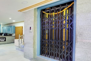 A hotel entrance with a metal gate, a reception desk, and a staircase leading to the interior.