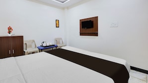 Ein Hotelzimmer mit einem Bett, einem an der Wand befestigten Fernseher, einem Schreibtisch mit Wasserkocher und einem Schrank.