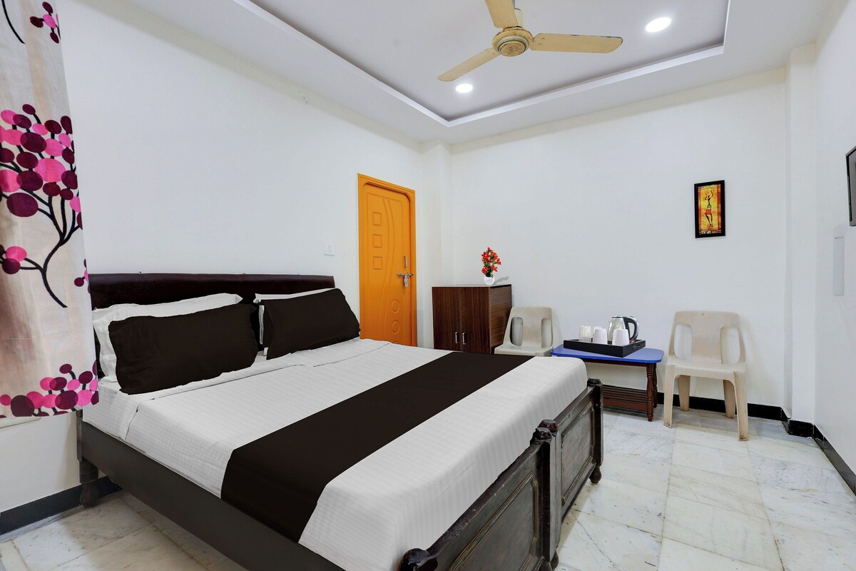 A hotel room with a bed, a desk, a chair, a wardrobe, a ceiling fan, and a door.