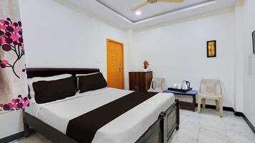 A hotel room with a bed, a desk, a chair, a wardrobe, a ceiling fan, and a door.