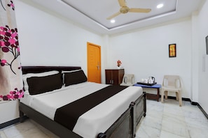 A hotel room with a bed, a desk, a chair, a wardrobe, a ceiling fan, and a door. - Super Hotel O Guntur Railway Junction (Guntur)