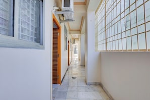 Un pasillo con piso de baldosas, una ventana con diseño de celosía y una unidad de aire acondicionado instalada en la pared.