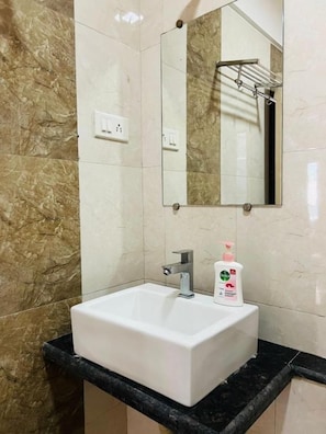 Un baño con lavamanos blanco, espejo y jabón de manos.