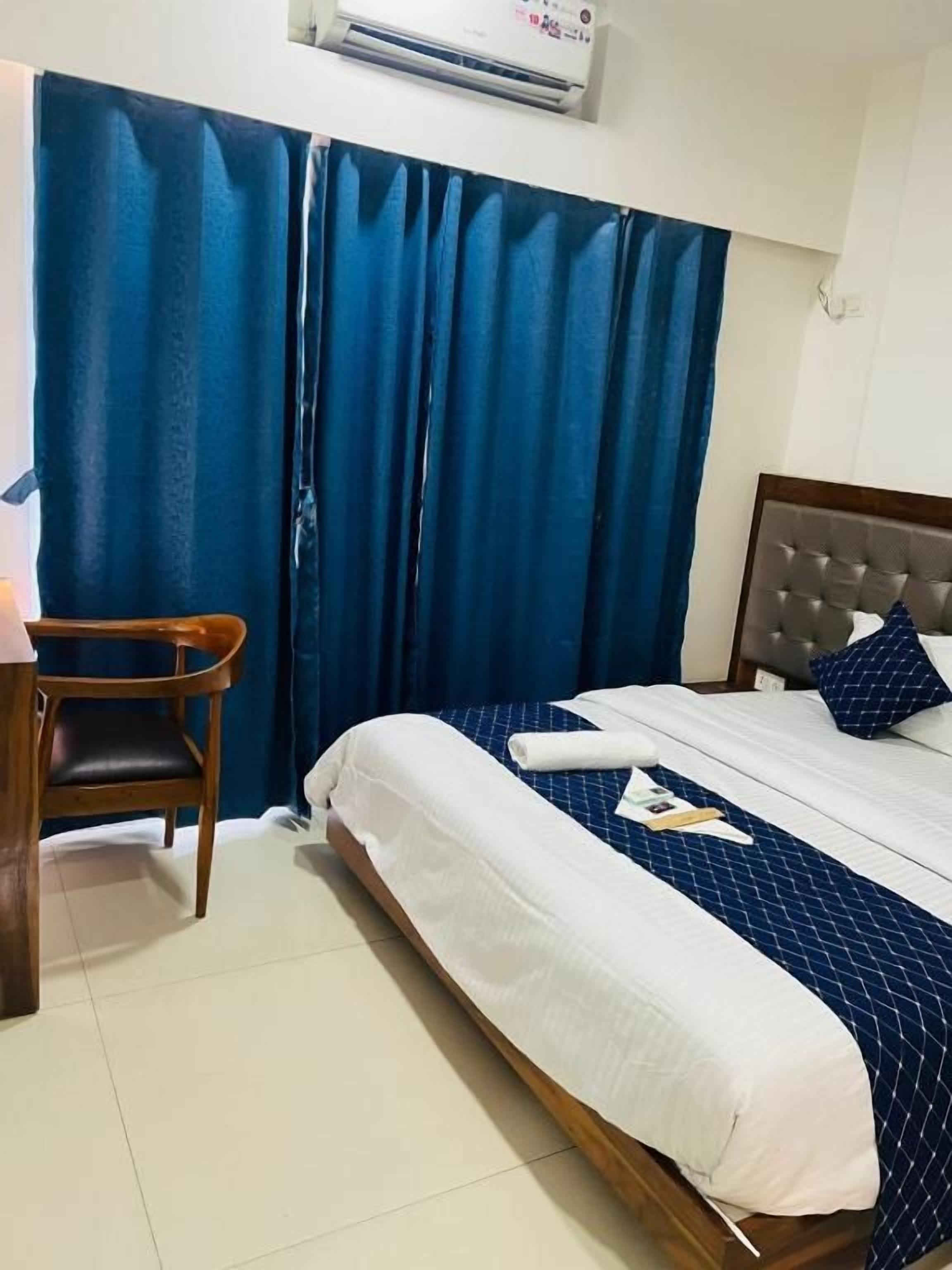 A hotel room with a bed, a chair, a desk, and a window with curtains.