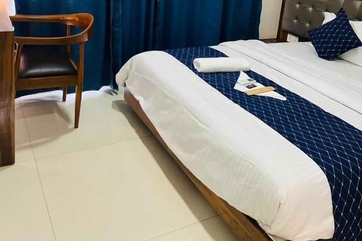 Una habitación de hotel con una cama, una silla, un escritorio y un ventanal con cortinas.