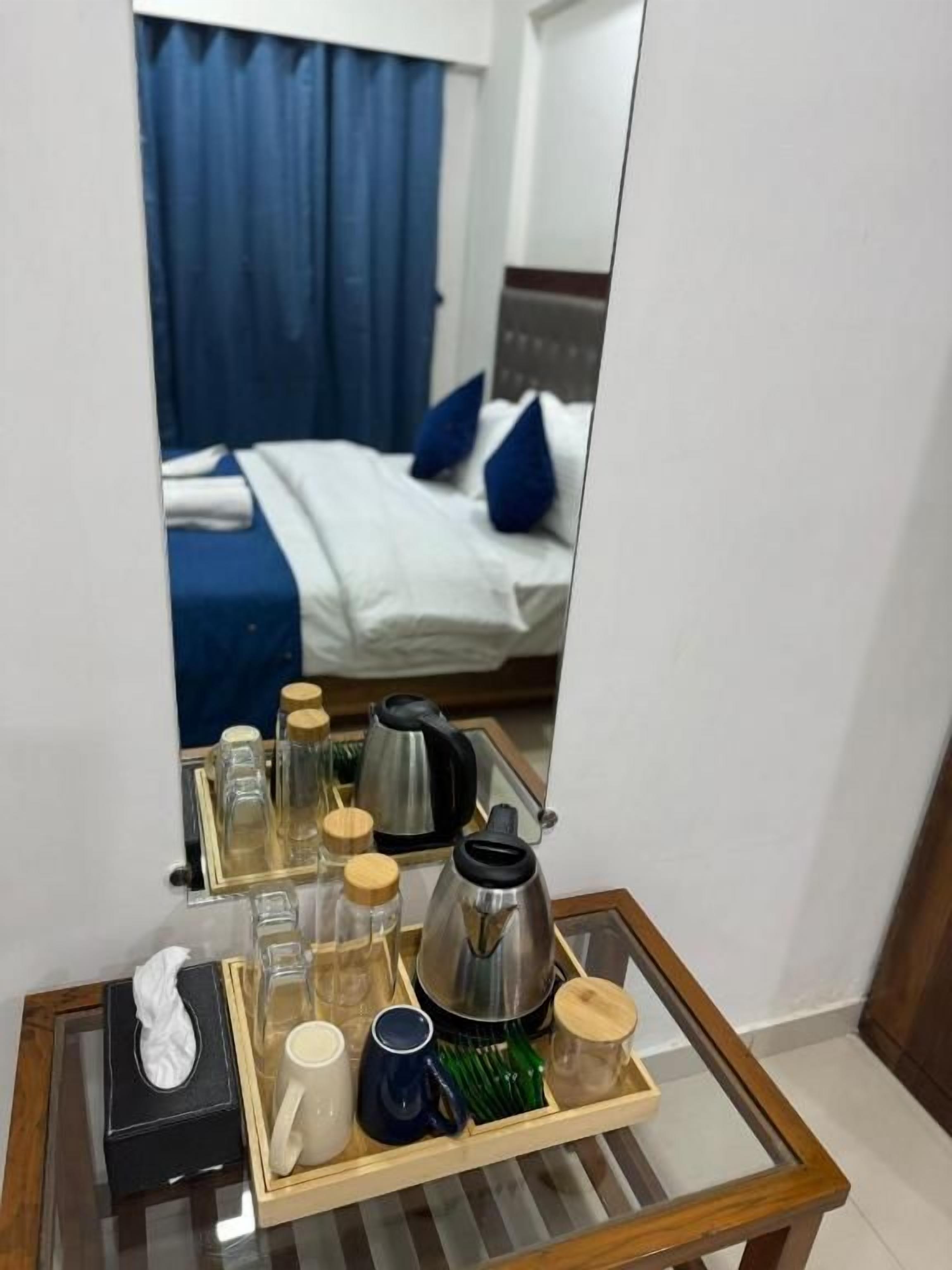 A hotel room with a bed, a bedside table with a tray of toiletries, and a mirror reflecting the room.