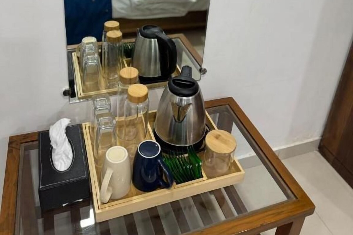 Habitación de hotel con una cama, una mesita de noche con un atrezo de artículos de aseo y un espejo que refleja la habitación.