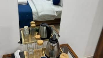 Quarto de hotel com cama, mesa de cabeceira e bandeja de artigos de higiene, além de espelho refletindo o ambiente.