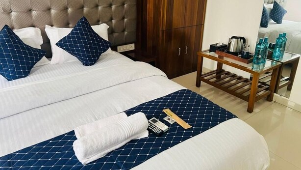 Habitación de hotel con cama, armario de madera, mesita de noche con hervidor y espejo que refleja la cama.