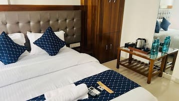 A hotel room with a bed, a wooden wardrobe, a bedside table with a kettle, and a mirror reflecting the bed.