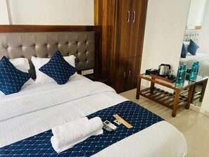 Habitación de hotel con cama, armario de madera, mesita de noche con hervidor y espejo que refleja la cama.