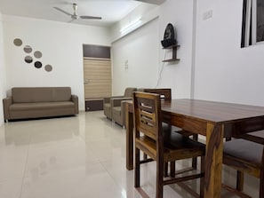 A dining area with a wooden table and chairs, a sofa, and a ceiling fan. - Luna Spaces Blues (Mumbai)