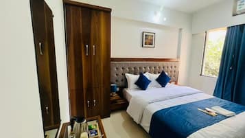 Quarto de hotel com cama, armário, mesa de cabeceira com luminária e janela com cortinas.