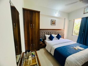 Quarto de hotel com cama, armário, mesa de cabeceira com luminária e janela com cortinas.