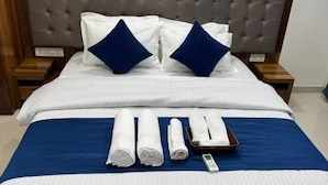 Ein ordentlich bezogenes Bett mit blauer Tagesdecke und weißen Laken, zwei Kissen sowie aufgerollte Handtücher an einem Holz-Kopfteil.