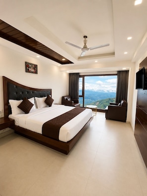 Habitación de hotel moderna con una cama grande, ventilador de techo, vistas a las montañas y un televisor de pantalla plana.