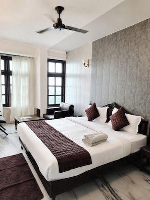 Habitación de hotel con una cama grande, ventilador de techo, escritorio y vistas al exterior.