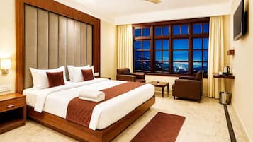 Habitación de hotel con una cama grande, un escritorio, una silla, un televisor y vistas de la ciudad de noche.