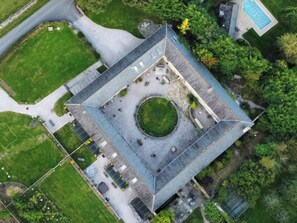 An aerial view of a square building with a central circular courtyard, surrounded by a paved area with benches and a small pool. - Halshanger Barn (Newton Abbot)