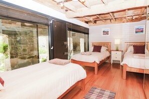 A room with two wooden beds, a stone wall, and a large window. - Halshanger Barn (Newton Abbot)