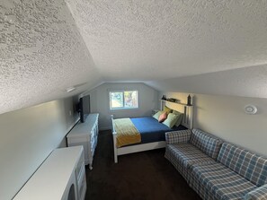 Ett sovrum med en säng, en tv, en byrå, ett fönster och en soffa.