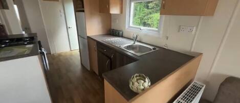 A compact kitchen with a sink, a stove, and a window overlooking greenery.