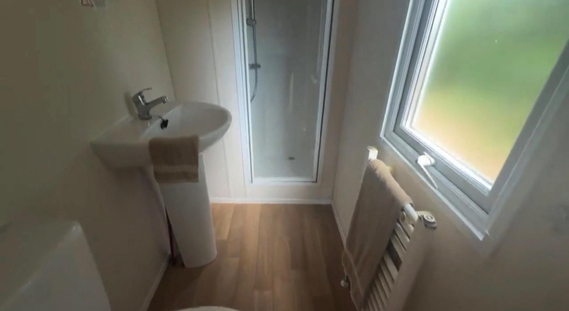 A small bathroom with a sink, a towel, a shower, and a window.