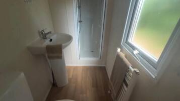 A small bathroom with a sink, a towel, a shower, and a window.