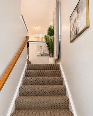 A staircase with patterned carpet, a wooden handrail, and a wall-mounted picture.