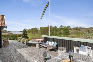 Eine Terrasse mit Gartenmöbeln, einer Flagge und Blick auf einen See und Grünflächen.