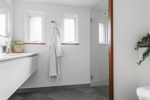 Un baño moderno con tocador blanco, bata colgada y zona de ducha.