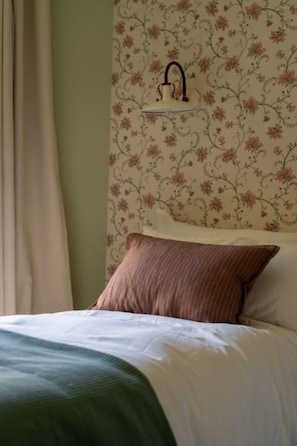 A bed with a green blanket, a brown pillow, and a floral wallpaper pattern.