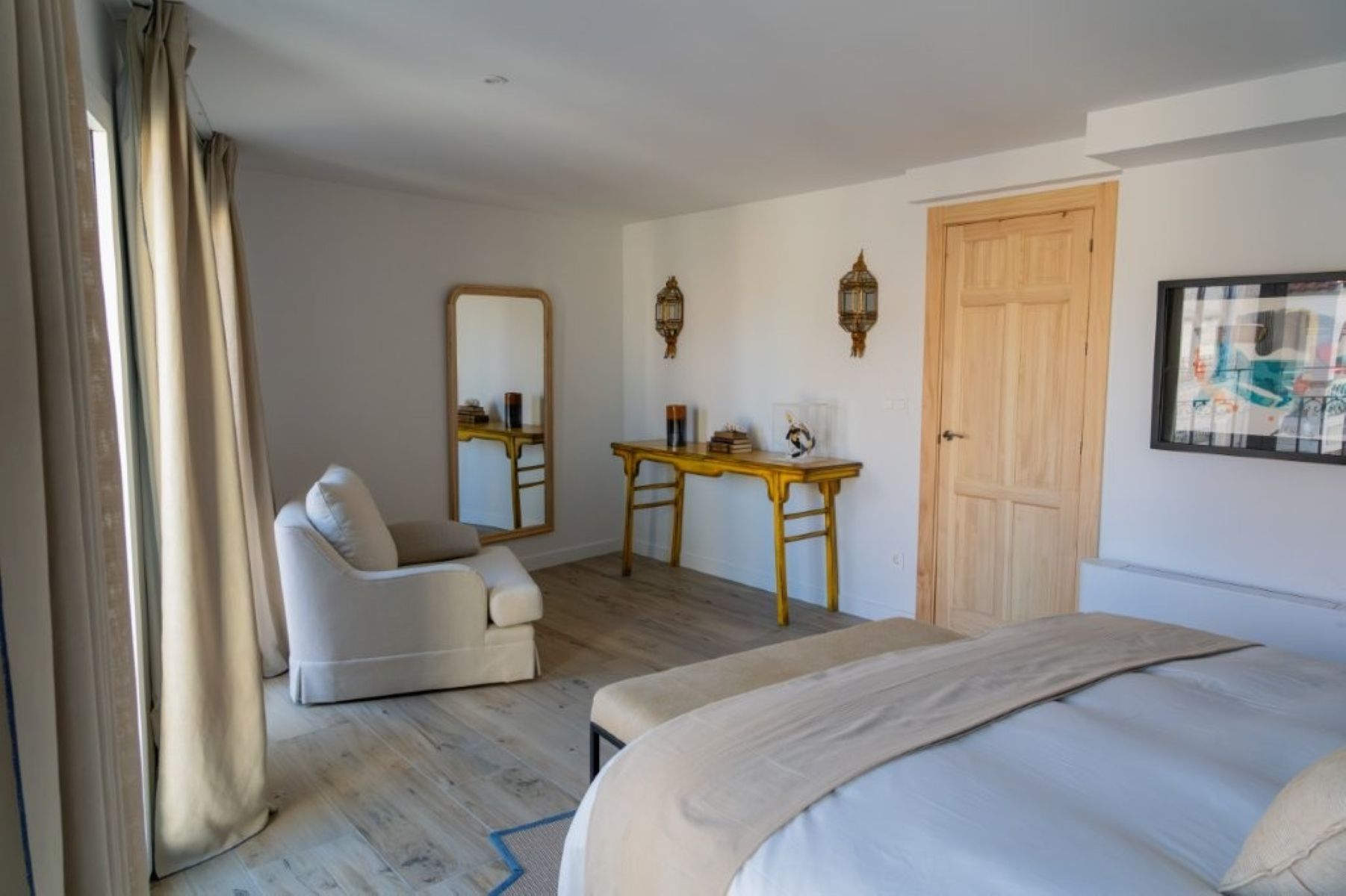 Una habitación de hotel con una cama, una silla, un escritorio, un espejo y una puerta.